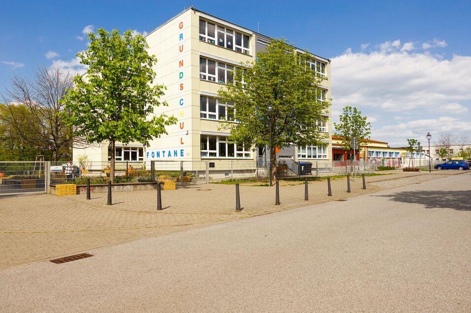 Schulgebäude der Grundschule Fontane mit Bäumen und Gehweg unter blauem Himmel in einer ruhigen Umgebung.