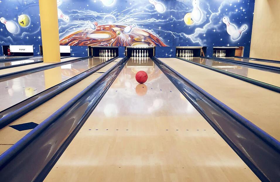 Blick auf eine Bowlingbahn mit einem roten Bowlingball in der Mitte und bunten Wandmalereien im Hintergrund.