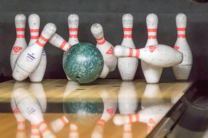 Gr&uuml;ne Bowlingkugel rollt auf eine Gruppe von zehn Bowlingpins auf einer Holzbahn.