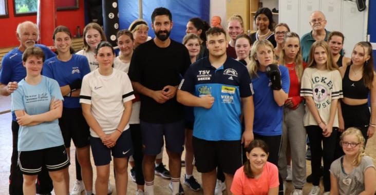 Gruppenshot von Jugendlichen und Trainern in einem Sportraum, alle in sportlicher Kleidung, l&auml;chelnd und posierend.
